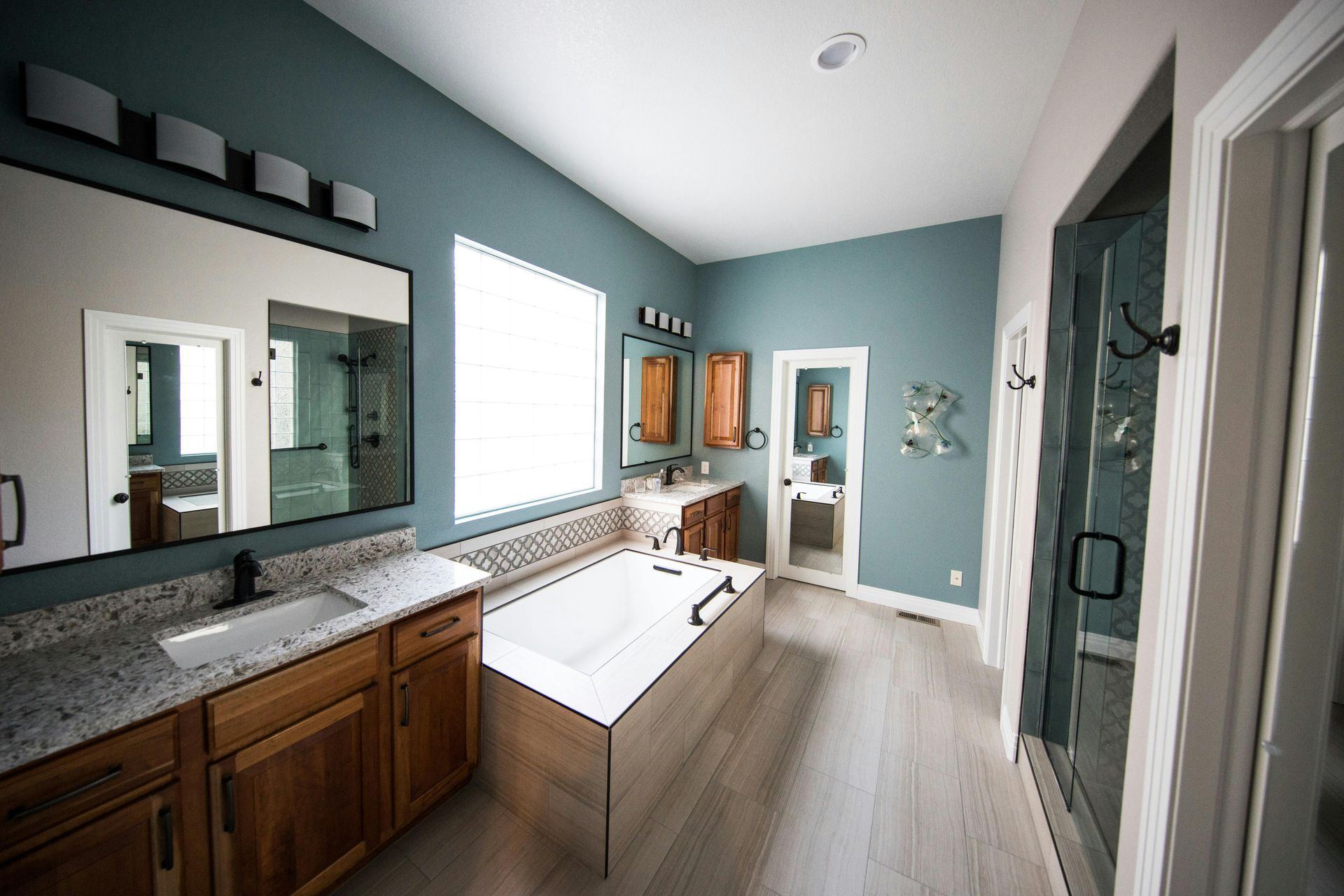 Spacious bathroom with a bathtub, vanity, and a shower, painted in blue and wood tones.