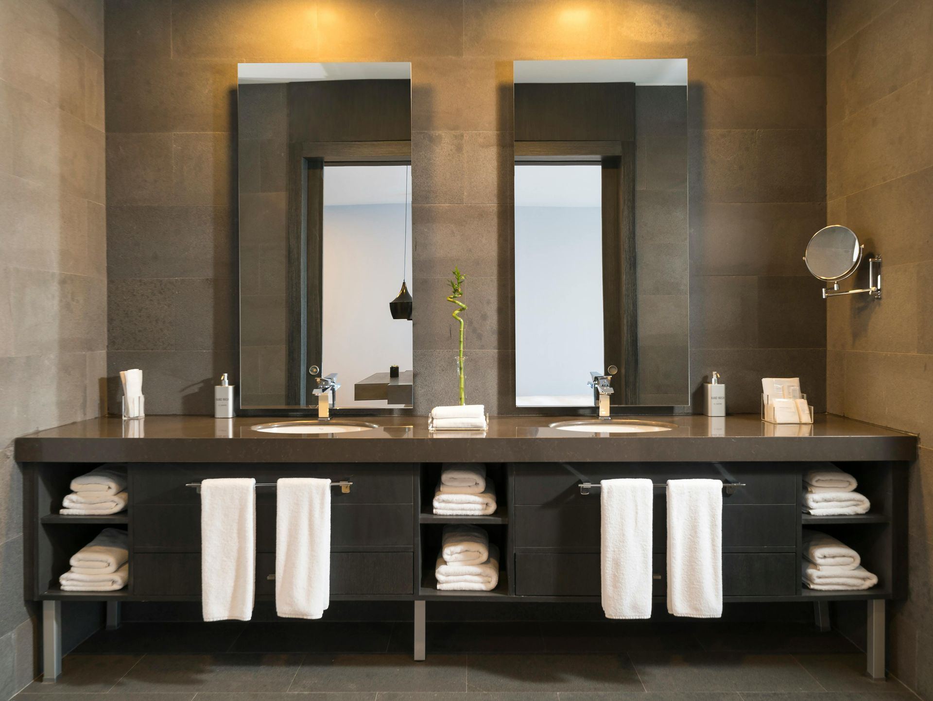 Modern bathroom with a double vanity, large mirrors, and gray tile. White towels are displayed.
