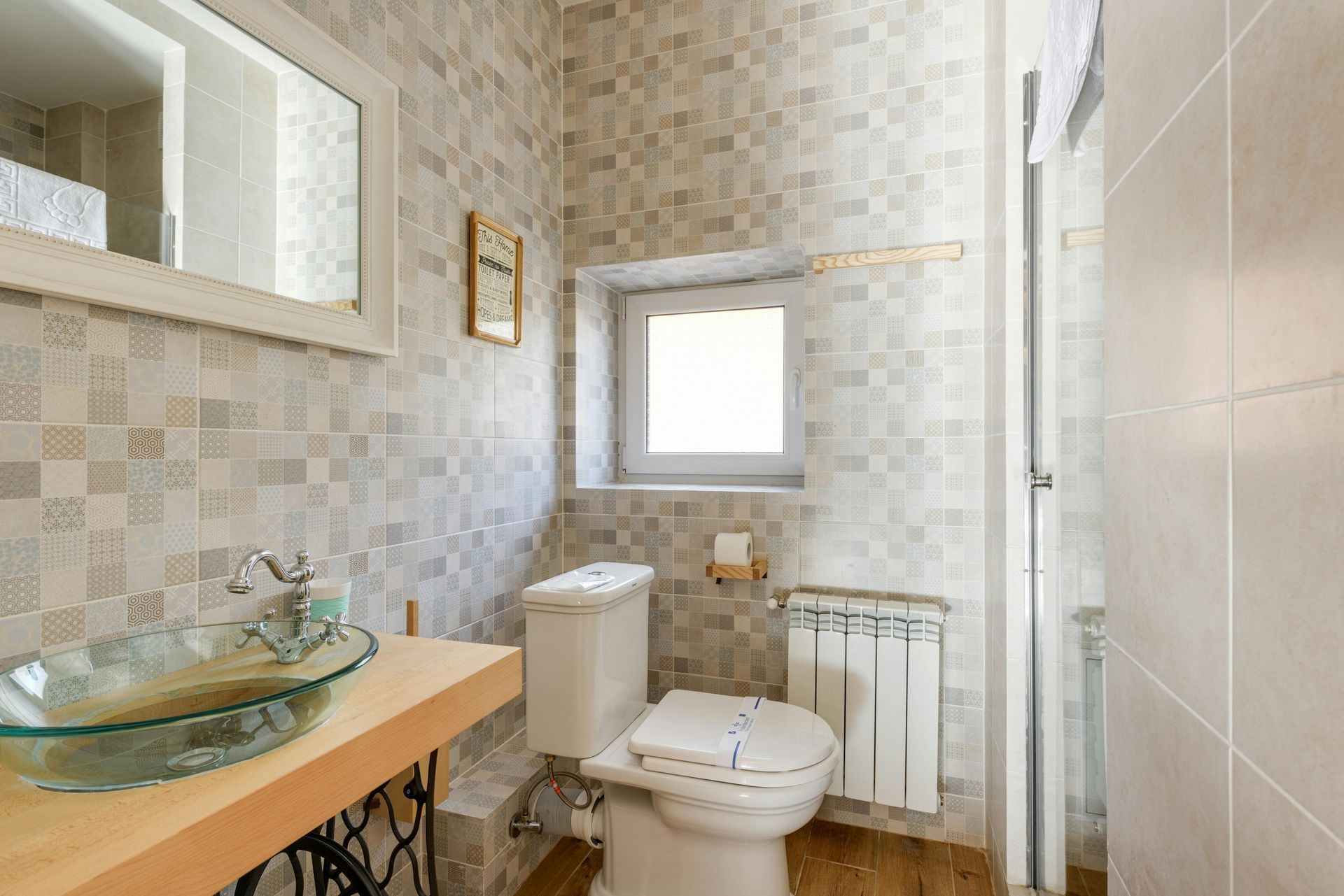 Bathroom with a glass sink, toilet, window, and tiled walls and floor.